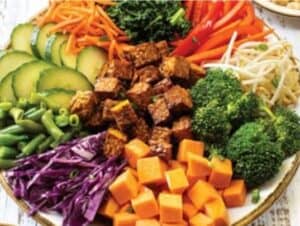 A vibrant, plant-powered platter brimming with sliced cucumbers, shredded carrots, red bell peppers, bean sprouts, green beans, broccoli, diced sweet potatoes, chopped purple cabbage, and leafy greens—all complemented by protein-rich cubed tofu.