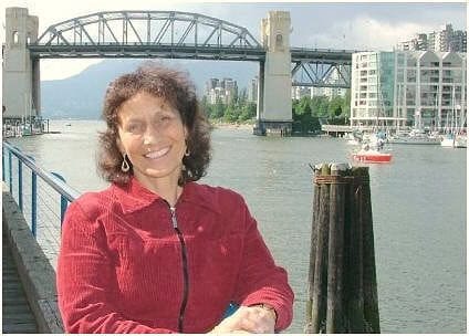 Woman smiling outdoors near water with bridge and cityscape in background.